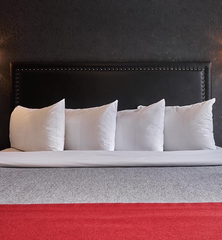 Four pillows on king bed neatly arranged with black wallpaper
