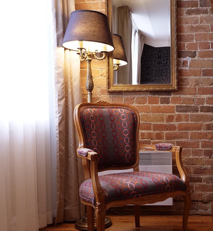 Antique chair and lamp with a mirror and brick wall at Hotel Bonaparte in Old Montreal